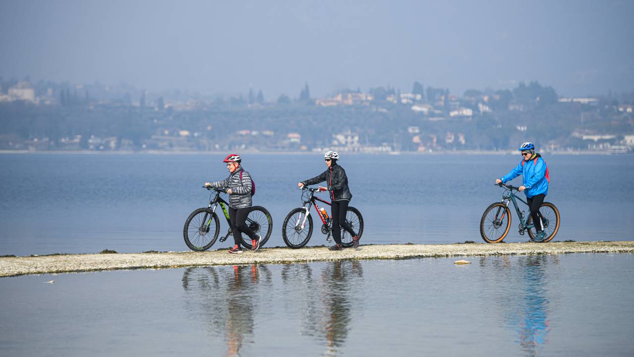 People walk towards the small island of San Biagio, off Manerba del Garda, Lake Garda, on February 21, 2023, where the water level dropped to its lowest in 30 years during the winter months. - A lack of snow on the surrounding mountain peaks, the absence of rain for the past six weeks, and mild temperatures - this explosive cocktail has caused the water level of Italy's largest lake to drop to its lowest in 30 years during the winter months. (Photo by Piero CRUCIATTI / AFP)