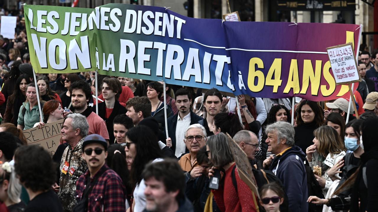 Protesters gather, holding a banner which reads as "Young people say no to pension at 64 year-old", as they take part in a demonstration on a national action day, a week after the government pushed a pensions reform through parliament without a vote, using the article 49.3 of the constitution, in Bordeaux, western France, on March 23, 2023. - French President defiantly vowed to push through a controversial pensions reform on March 22, 2023, saying he was prepared to accept unpopularity in the face of sometimes violent protests. (Photo by Philippe LOPEZ / AFP)