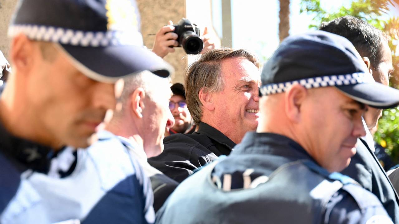 Former Brazilian president Jair Bolsonaro, surrounded by police officers, greets supporters at the Liberal Party headquarters in Brasilia on March 30, 2023. - Disconsolate over his "unjust" defeat in Brazil's divisive 2022 elections, Bolsonaro was uncharacteristically quiet when he slipped out of Brazil in the twilight of his presidential term for a self-imposed exile in Florida. (Photo by Evaristo Juliano DE SA and EVARISTO SA / AFP)