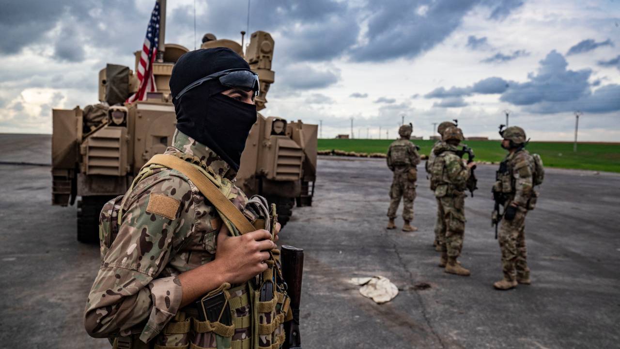 A member of the Syrian Democratic Forces (SDF) (L) and US soldiers are pictured near an armoured military vehicles are pictured on the outskirts of Rumaylan in Syria's northeastern Hasakeh province, bordering Turkey, on March 27, 2023. (Photo by Delil souleiman / AFP)