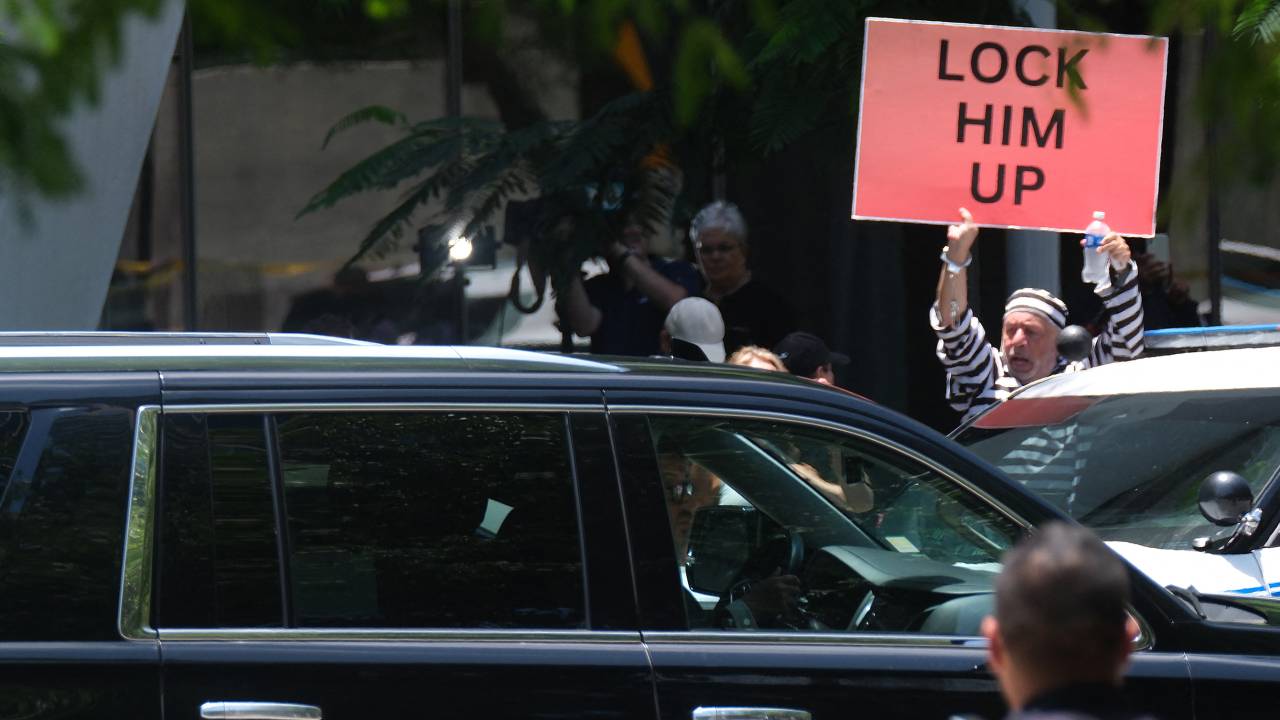 A demonstrator holds a sign as a motorcade of vehicles, with former US President Donald Trump on board, arrives at Wilkie D. Ferguson Jr. United States Federal Courthouse in Miami, Florida, on June 13, 2023. Trump is appearing in court in Miami for an arraignment regarding 37 federal charges, including violations of the Espionage Act, making false statements, and conspiracy regarding his mishandling of classified material after leaving office. (Photo by RICARDO ARDUENGO / AFP)