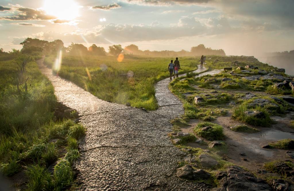 Tourists walk along a pathway at Victoria Falls which spray mist into the air contributing to the areas thick, lush vegetation. Mosi-oa-Tunya National Park, Zimbabwe VICTORIA FALLS, ZIMBÁBUE - O Parque Nacional Mosi-oa-Tunya, na fronteira com a Zâmbia, é uma das maiores quedas-d'água do mundo. Os viajantes passeiam e, simultaneamente, entendem o zelo com a fauna, composta de animais como elefantes e búfalos