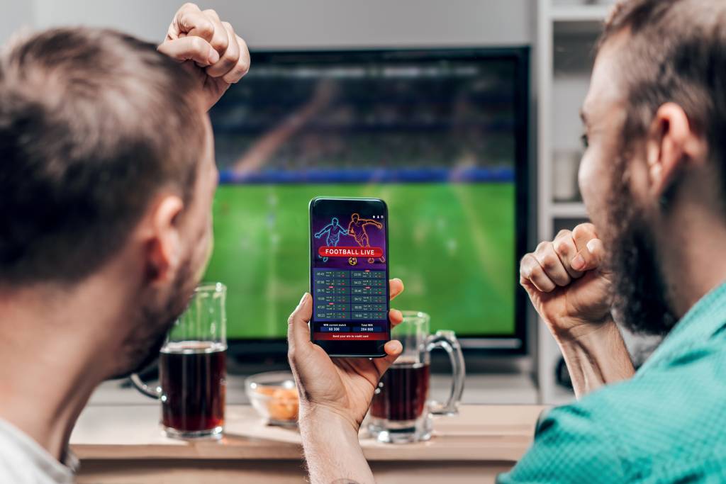 Two male friends watching live football game broadcast on tv EM CAMPO - Apostas esportivas: promessa de arrecadar 15 bilhões de reais