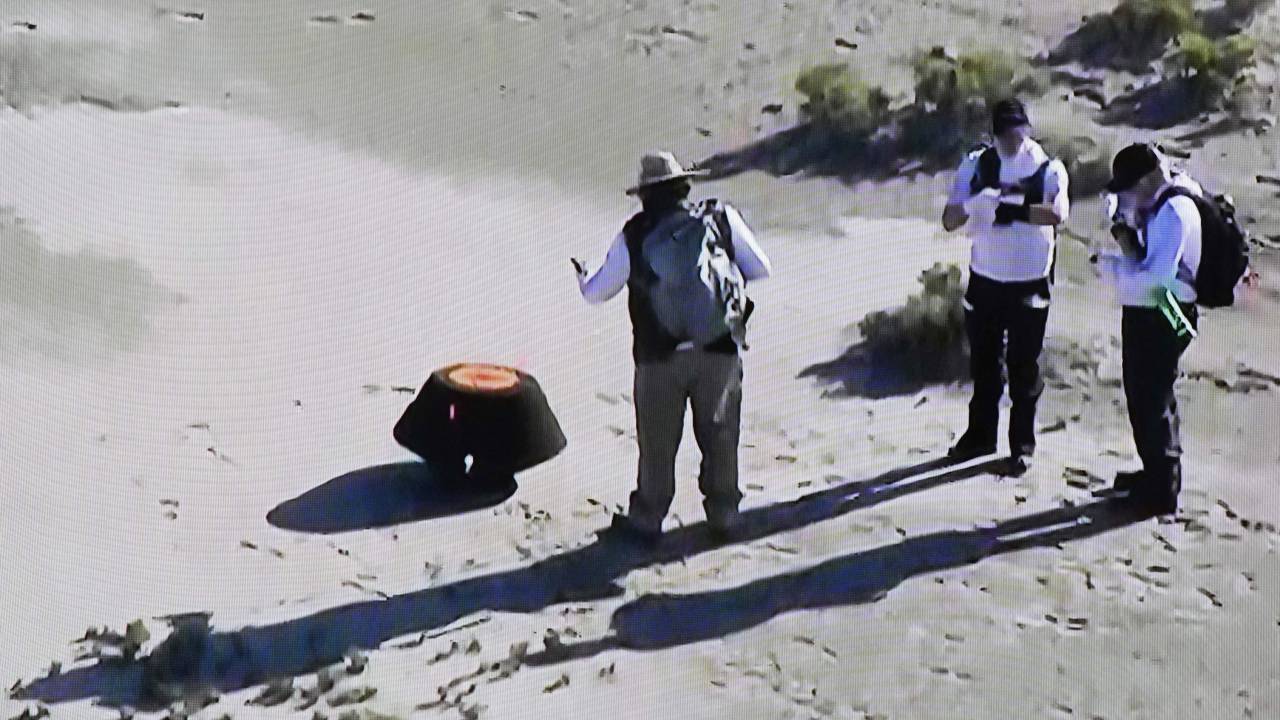 This shot off a NASA live feed shows NASA safety team members prepare the Osiris-Rex asteroid sample return craft sitting in the Utah desert at Dugway, Utah, on September 24, 2023. The largest sample ever collected from an asteroid in space, and the first for NASA, landed in the Utah desert Sunday after a fiery final descent through Earth's atmosphere, seven years after the mission's launch. Scientists hope the asteroid sample aboard the spacecraft will provide humanity with a better understanding on the formation of our solar system and how Earth became habitable. (Photo by Handout / NASA / AFP) / RESTRICTED TO EDITORIAL USE - MANDATORY CREDIT "AFP PHOTO / NASA " - NO MARKETING NO ADVERTISING CAMPAIGNS - DISTRIBUTED AS A SERVICE TO CLIENTS