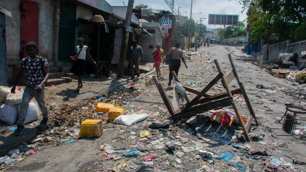 People walk past a barricade in a road in Port-au-Prince, Haiti, on March 20, 2024. Negotiations to form a transitional council to govern Haiti advanced on March 20, as the United States airlifted more citizens to safety from gang violence that has plunged the impoverished country into chaos. (Photo by Clarens SIFFROY / AFP)