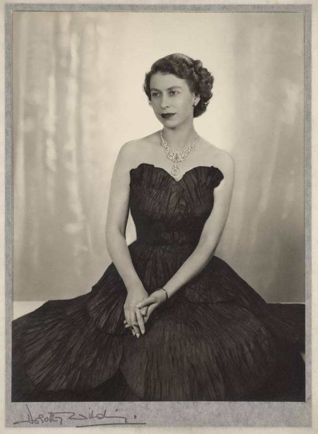 Rainha Elizabeth Os Correios e a Casa da Moeda Real concederam a primeira foto da posse oficial da rainha Elizabeth II como monarca a Dorothy Wilding. O vestido de tafetá preto, a pose e a escolha das joias nesta sessão foram considerados inadequados para as necessidades dos comissários, o que motivou uma segunda sessão de fotos. Ocorrendo apenas 20 dias após a ascensão, a imagem de Wilding é uma visão sobre a formação da imagem da nova e jovem rainha. -