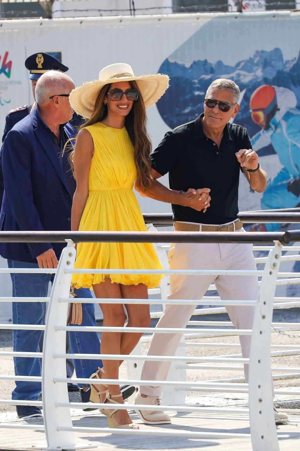 BGUS_3012676_014 Ela, de vestido amarelo, plissado de seda; ele de camisa polo e calça marfim
