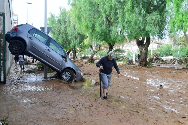 A resident walks next to a car lifted up in a street covered in mud in a flooded area in Picanya, near Valencia, eastern Spain, on October 30, 2024. Floods triggered by torrential rains in Spain's eastern Valencia region has left 51 people dead, rescue services said on October 30. (Photo by Jose Jordan / AFP)