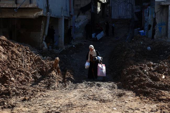 PALESTINIAN-ISRAEL-WAR A woman carries belongings as she walks across a destroyed street while fleeing the Nur Shams camp for Palestinian refugees near Tulkarem, where Israeli forces allowed residents to retrieve belongings after issuing reported demolition notifications for several houses, amid a weeks-long offensive in the occupied West Bank on February 26, 2025. (Photo by Zain JAAFAR / AFP)