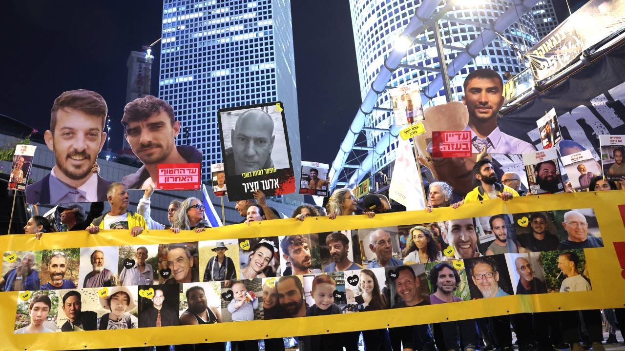 Friends and relatives of Israeli hostages held captive since the October 7 attacks by Palestinian militants in the Gaza Strip, stand behind a banner bearing their portraits during a demonstration calling for action to secure their release in front of the Israeli Defense Ministry in Tel Aviv on March 11, 2025. (Photo by Jack GUEZ / AFP)