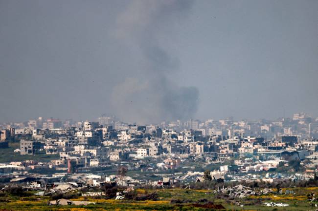 A cloud of smoke billows as destroyed buildings are pictured in the northern Gaza Strip from across the border in southern Israel on March 18, 2025. Israel on March 18 unleashed its most intense strikes on the Gaza Strip since a January ceasefire, with rescuers reporting 220 people killed, and Hamas accusing Benjamin Netanyahu of deciding to 