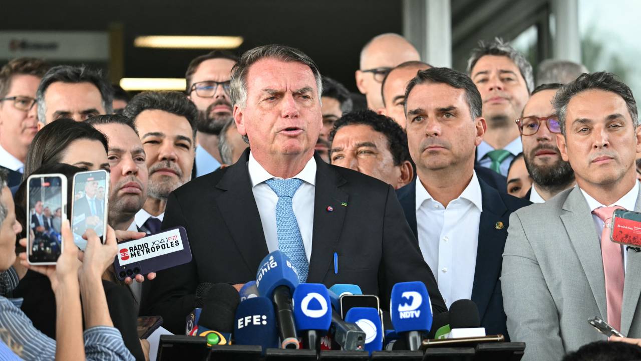 Former Brazil's President Jair Bolsonaro speaks to the media next to his son Senator Flavio Bolsonaro (C-Right), after leaving the Senate building in Brasilia on March 26, 2025. Brazil's Supreme Court on March 26, 2025, ordered far-right ex-president Jair Bolsonaro to stand trial on charges of plotting a coup after failing to win re-election in 2022. (Photo by EVARISTO SA / AFP)