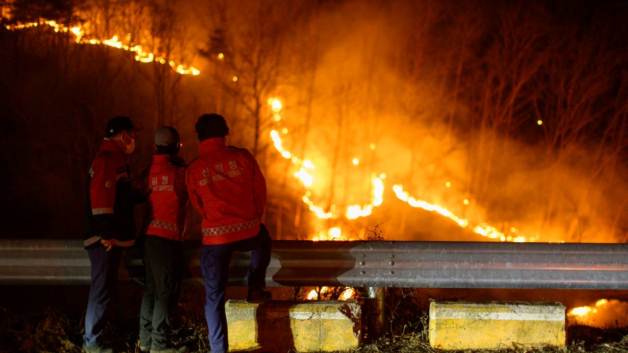 Bombeiros observam as chamas se alastrarem em incêndio florestal na cidade de Andong, na Coreia do Sul. 27/03/2025