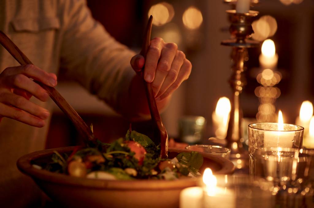Man taking salad from bowl at candlelight dinner HORA DO COMIDA - Balanço: o jantar realmente pede refeições mais leves