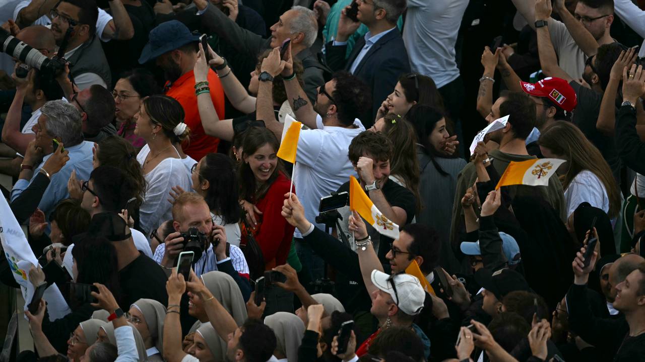 People react and wave Vatican flags as white smoke (unseen) signals that cardinals elected a new pope during their conclave in the Vatican on May 8, 2025. (Photo by Gabriel BOUYS / AFP)