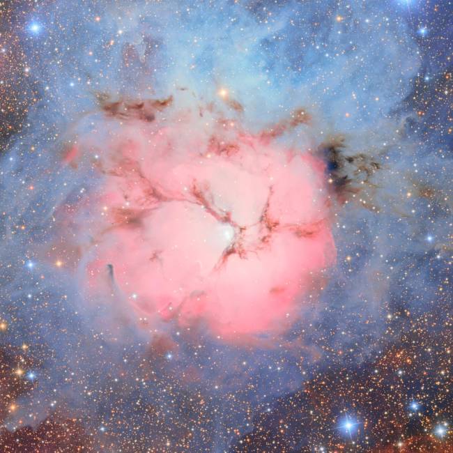 A nebulosa Trífida é uma combinação incomum de um aglomerado aberto de estrelas, uma nebulosa de emissão com nuvens brilhantes de gás e poeira que emitem luz própria (região rosa), uma nebulosa de reflexão que reflete a luz de estrelas próximas (região azul) e uma nebulosa escura tão densa que bloqueia a luz dos objetos ao fundo (regiões escuras).