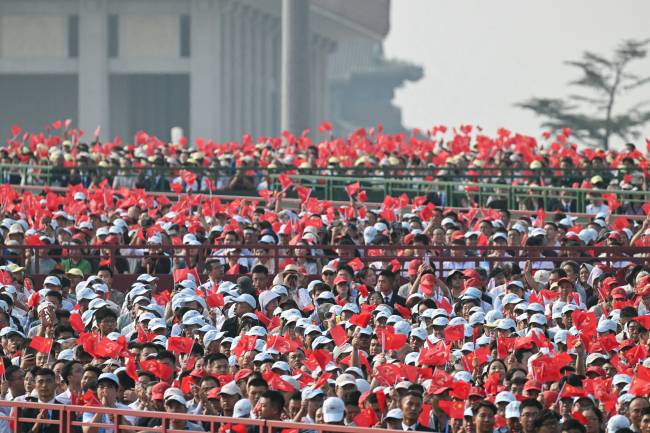 Attendees wave flags in the stands as songs play in the background before a military parade marking the 80th anniversary of victory over Japan and the end of World War II, in Beijing’s Tiananmen Square on September 3, 2025. (Photo by Greg Baker / AFP)