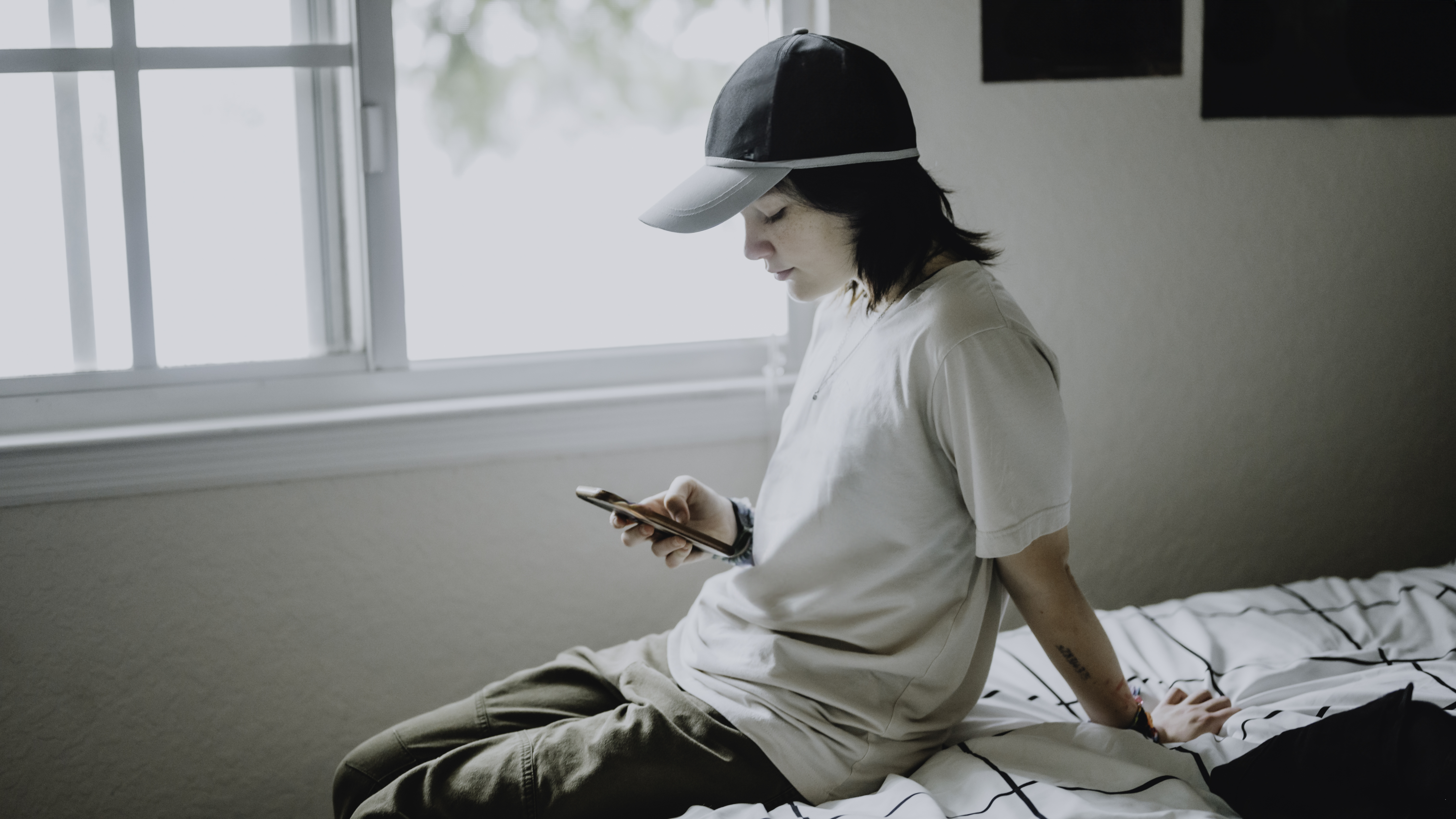 Transgender non-binary teenager at home in their bedroom using cellphone