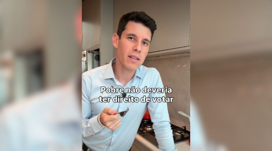 Homem branco de camisa social azul clara, com cabelo escuro e curto, segurando uma colher de metal na mão direita, em uma cozinha moderna. O texto sobreposto diz: Pobre não deveria ter direito de votar