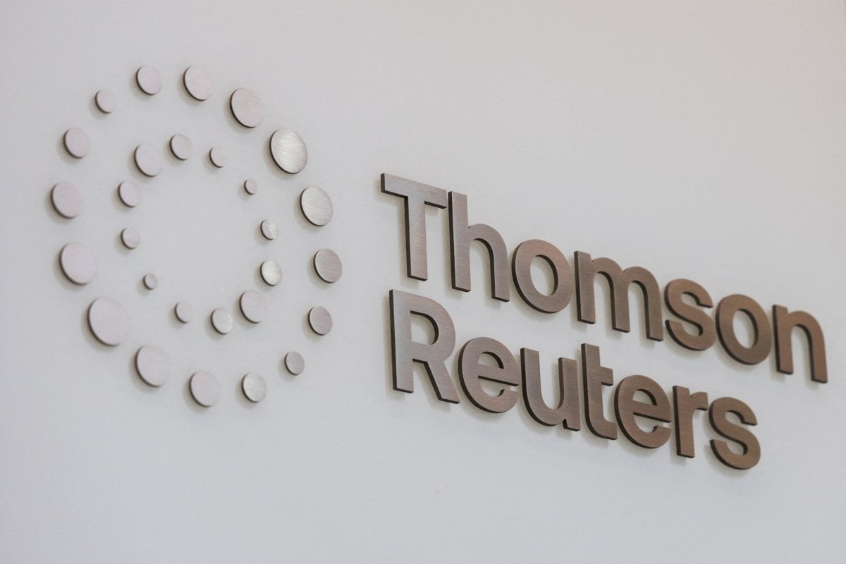 Logotipo da Thomson Reuters em relevo na parede branca, com o nome da empresa em letras marrons e um símbolo circular de pontos prateados