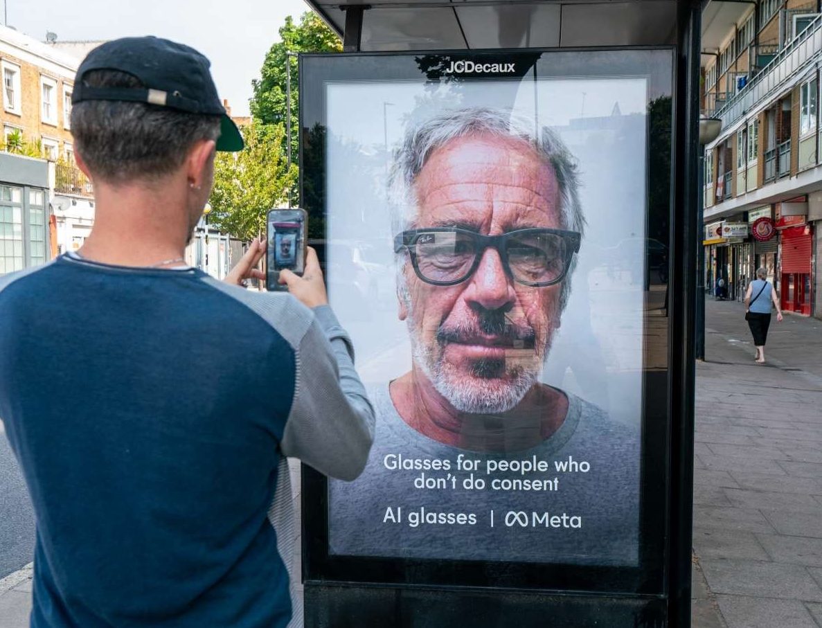 Homem de boné preto e blusa azul e cinza fotografa um outdoor em ponto de ônibus na Carnegie Street. O anúncio exibe o rosto de um homem barbudo de óculos e o texto Glasses for people who dont do consent AI glasses | Meta